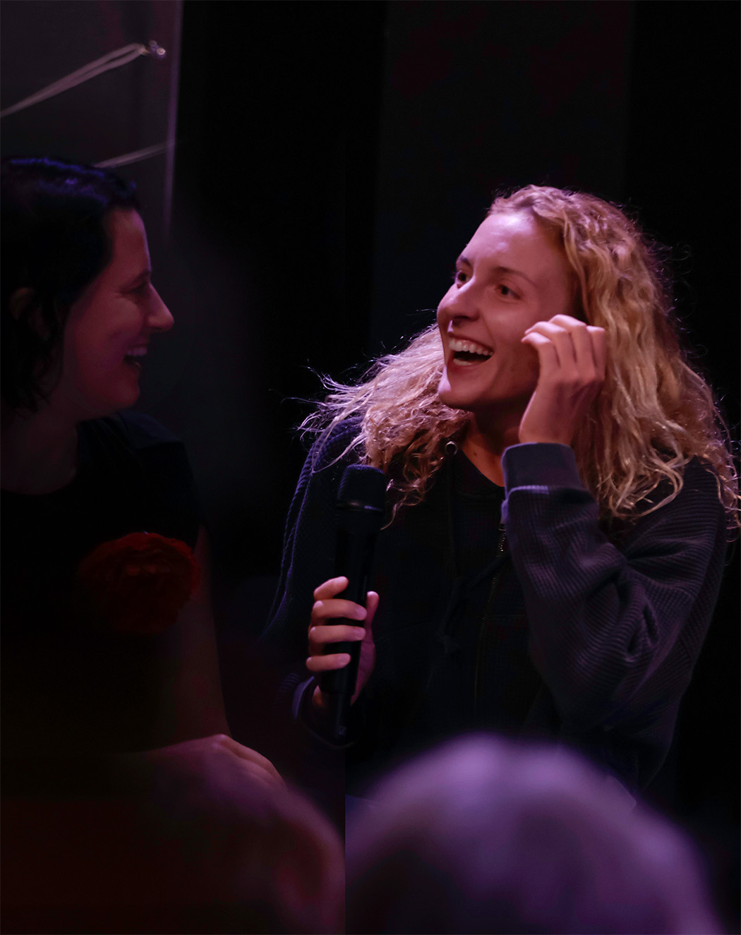 A performer with curly hair laughing while holding a microphone