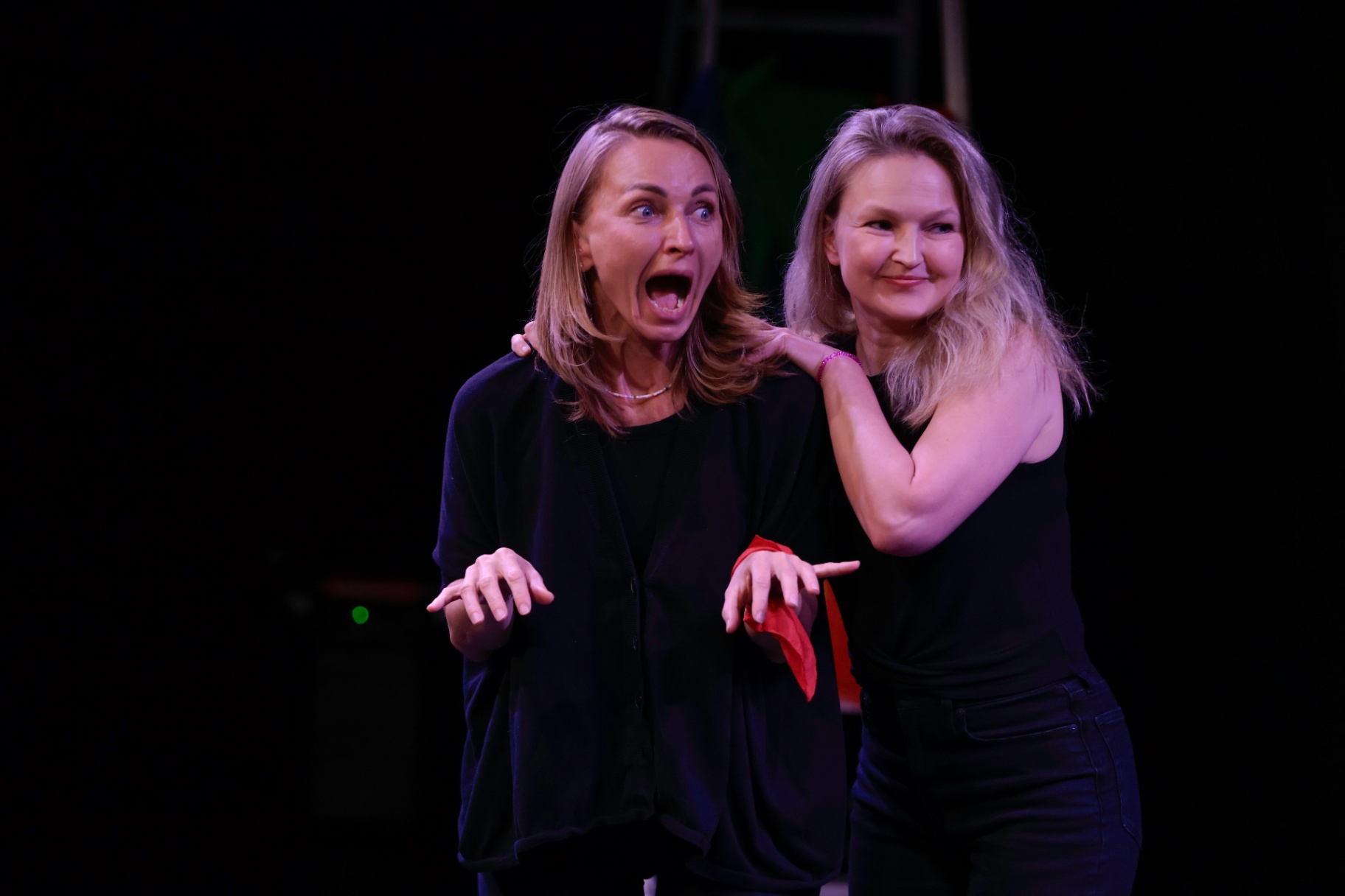Two performers, one wide-mouthed in shock, the other grinning behind her