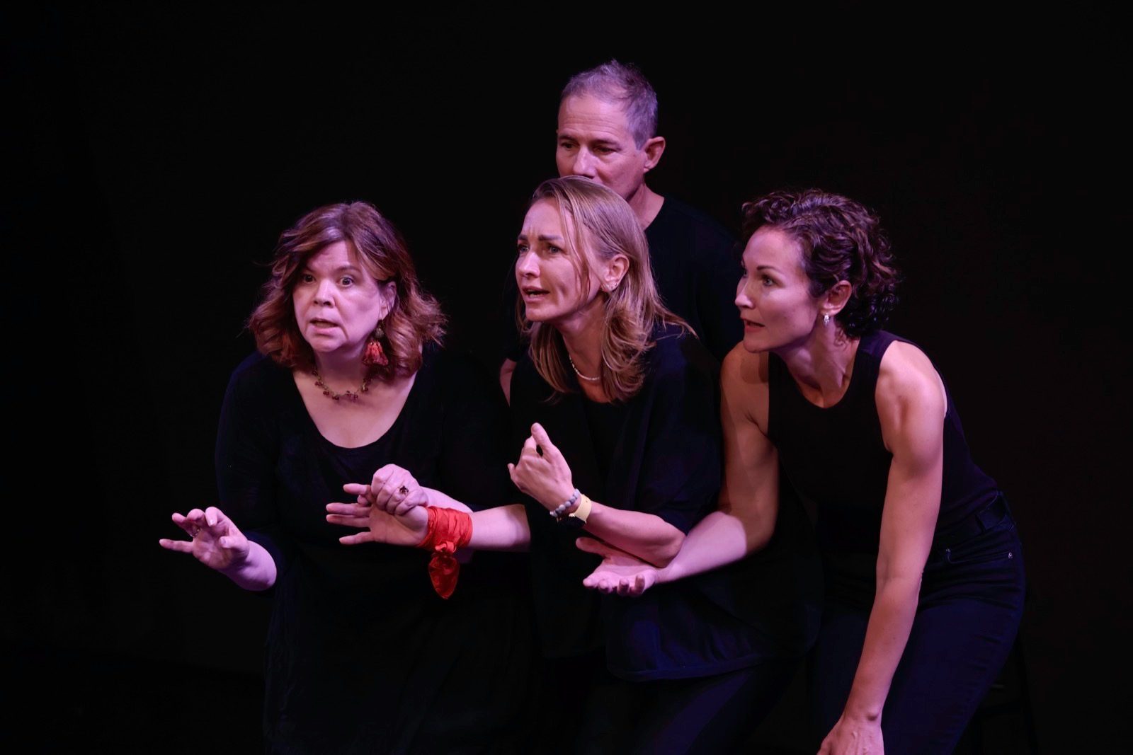Four performers in black respond with expressive faces